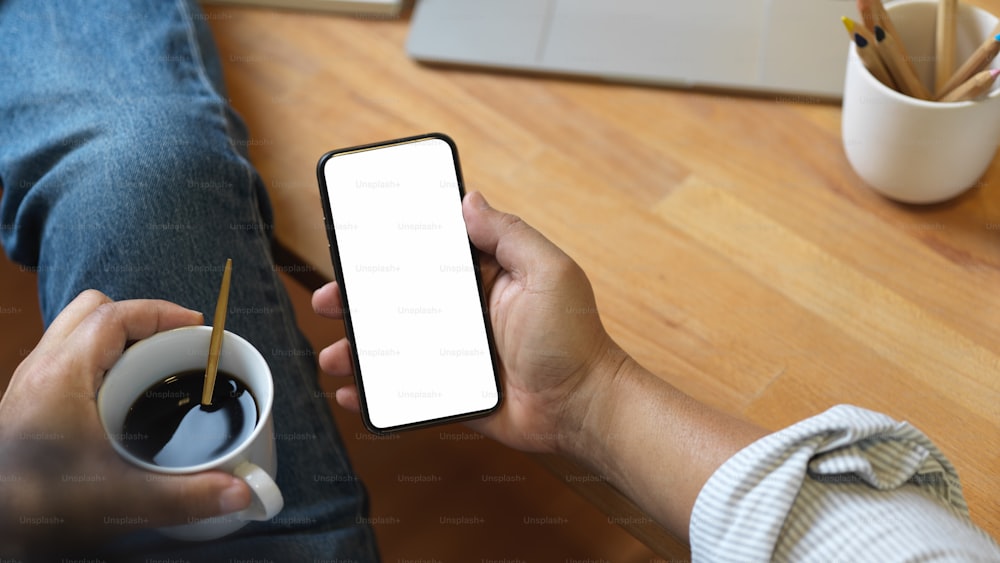 Close up view of male hand holding smartphone and coffee cup while relaxed sitting in office room