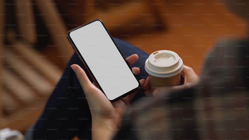 Close up view of female hand holding smartphone and paper cup while relaxed sitting in office room