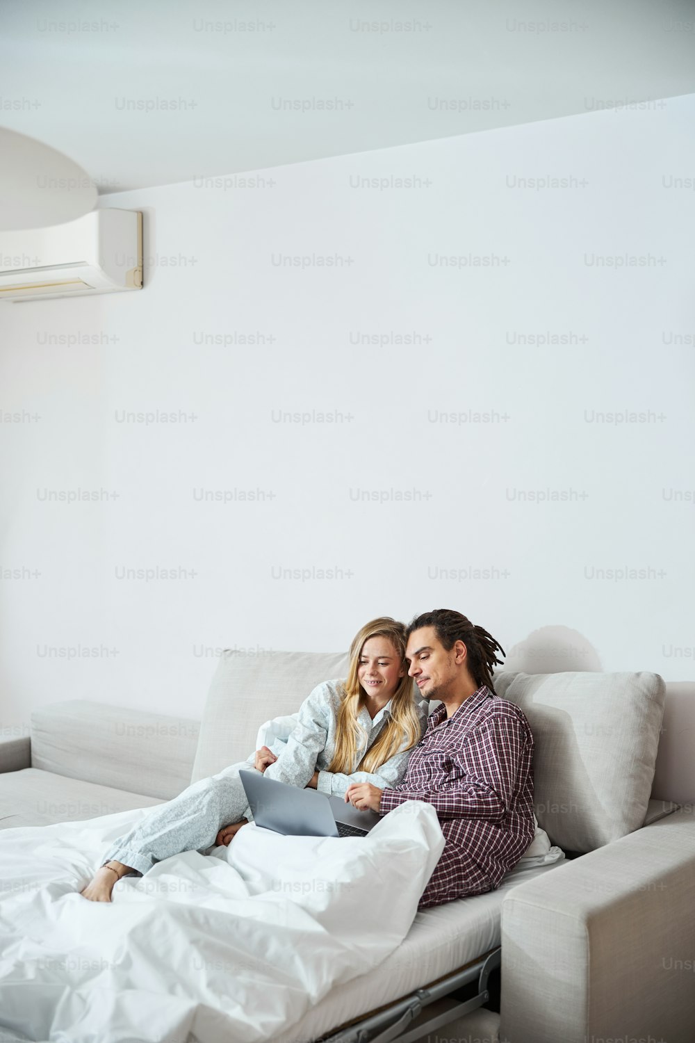 Charming young woman in pajamas cuddling with boyfriend and smiling while watching movie on notebook