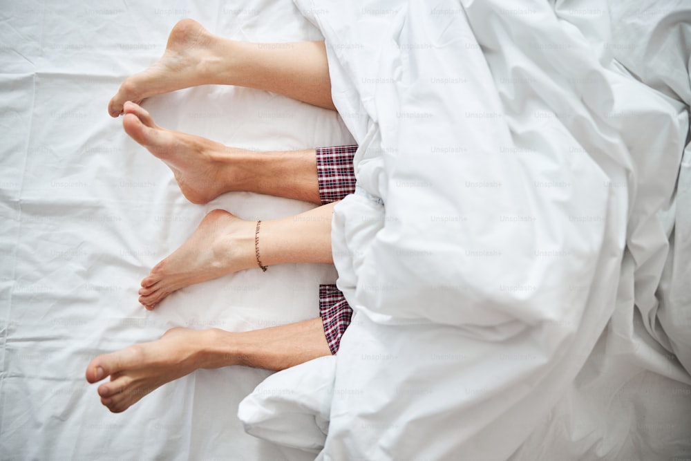 Close up of girlfriend and boyfriend with bare feet resting under white blanket at home