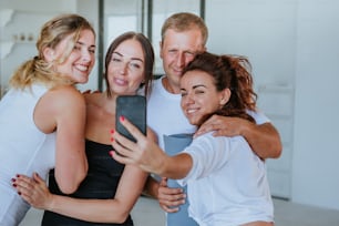 Smiling young people having fun making selfie photo after yoga class indoor.