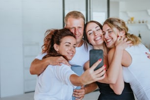 Jóvenes sonrientes que se divierten haciendo fotos selfie después de la clase de yoga en el interior.
