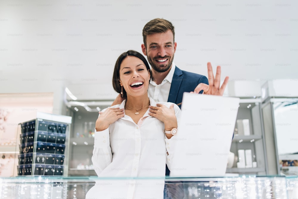 Beautiful couple enjoying in shopping at modern jewelry store. Young woman try it out gorgeous necklace and earrings.