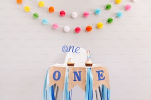 Festive background decoration for birthday celebration. Letters text one and one candle in small cupcakes for baby child birthday. Garland decoration on background. Cake smash first year.