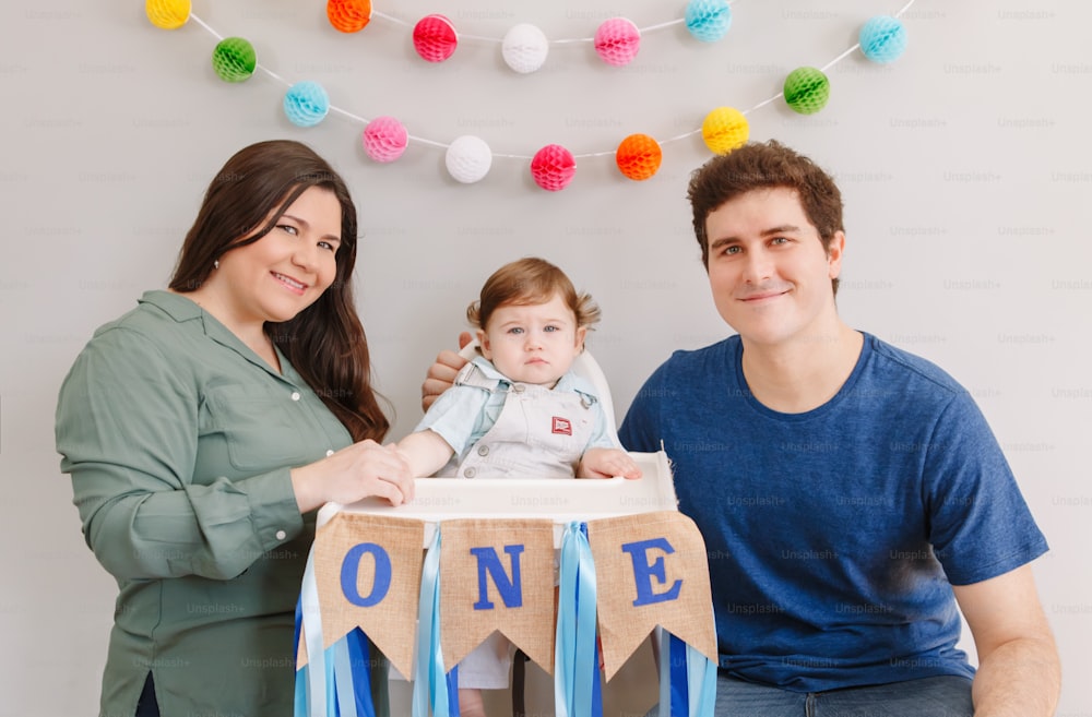Caucasian family with baby boy celebrating his first birthday at home. Proud parents mother and father dad together with child kid toddler. Happy birthday lifestyle concept.
