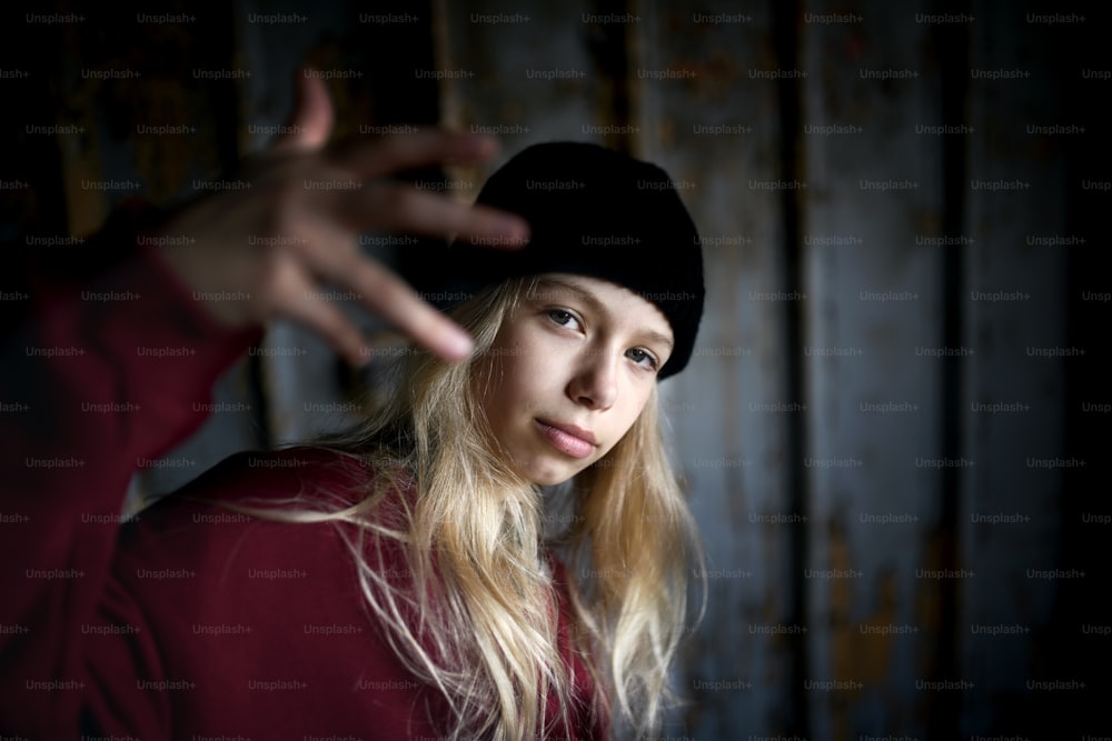 Front view portrait of blond teenager girl standing indoors in abandoned building.