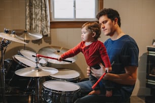 아버지가 아기에게 드럼 연주를 가르치고 있다. 유아 자녀를 둔 부모는 함께 즐거운 시간을 보내고 있습니다. 아빠와 아이가 음악을 연주하고 있다. 가족 취미 활동 및 여가 시간.