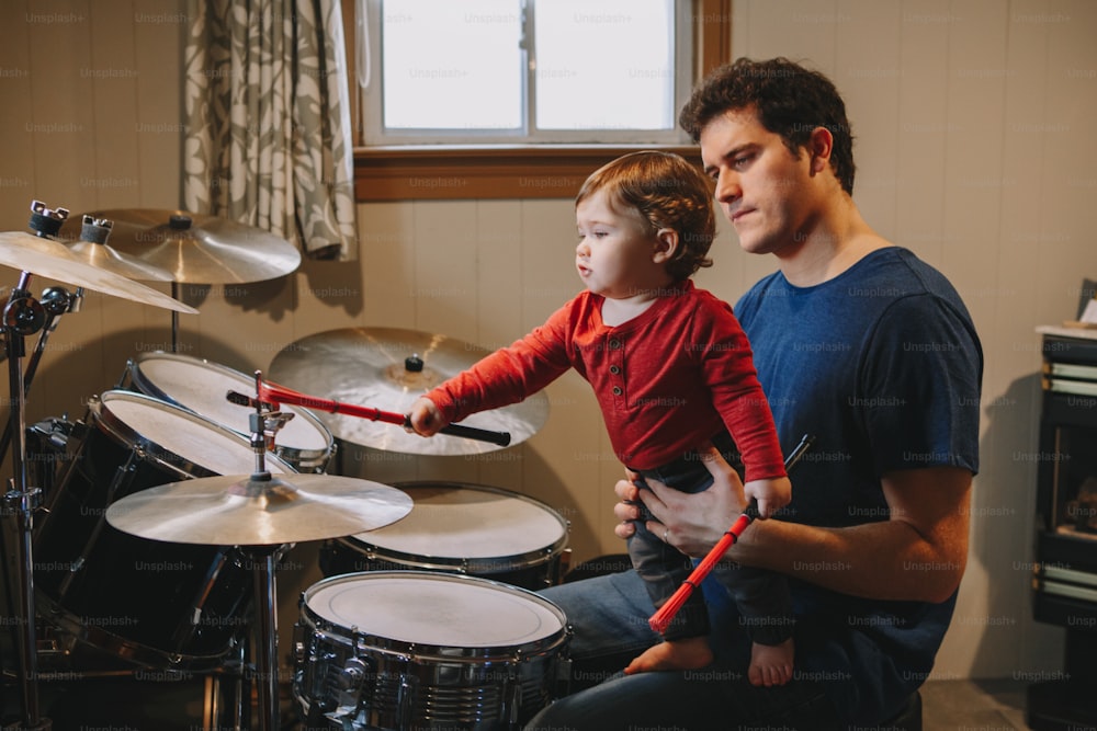 Pai ensinando o menino a tocar bateria. Pai com criança pequena se divertindo e passando tempo juntos. Pai e criança tocando música. Atividade de passatempo em família e tempo de lazer.