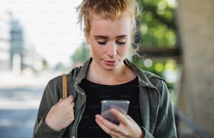 Portrait de face d’une jeune femme aux cheveux roux à l’extérieur en ville, à l’aide d’un smartphone.