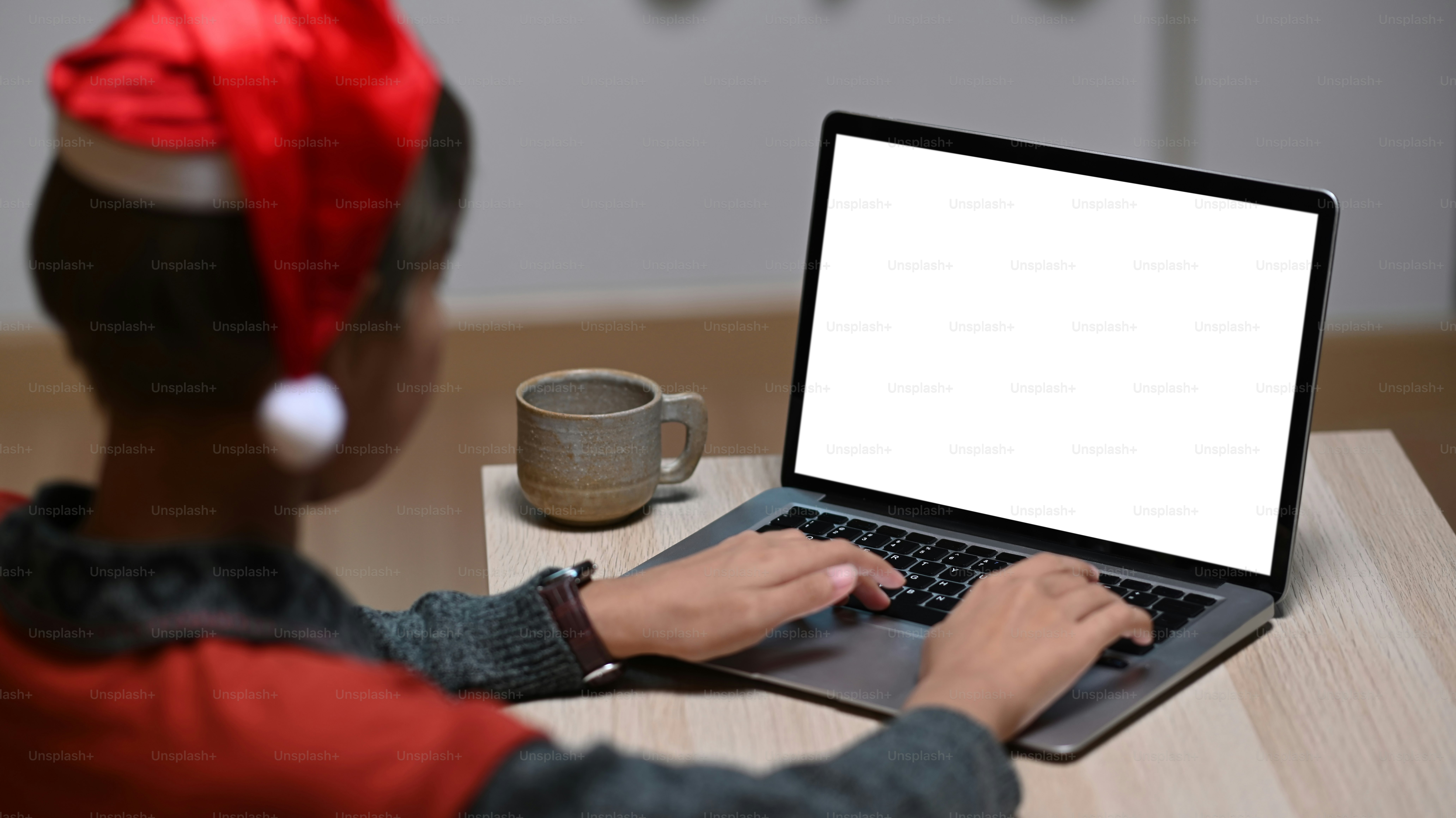A designer woman in Christmas hat is working on laptop with blank screen in office.