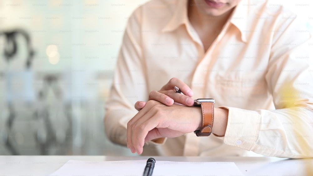 Foto recortada de un hombre de negocios está mirando un reloj inteligente en su mano.