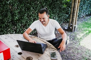 Latin Man working with laptop outdoor in a beautiful terrace using smartphone and computer sitting cross-legged in Home work in Mexico City
