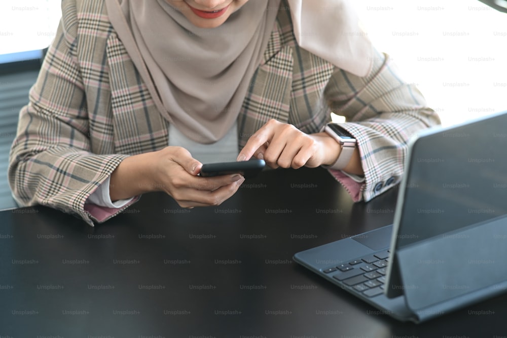Cropped shot of happy muslim woman using mobile phone while sitting at her workplace.