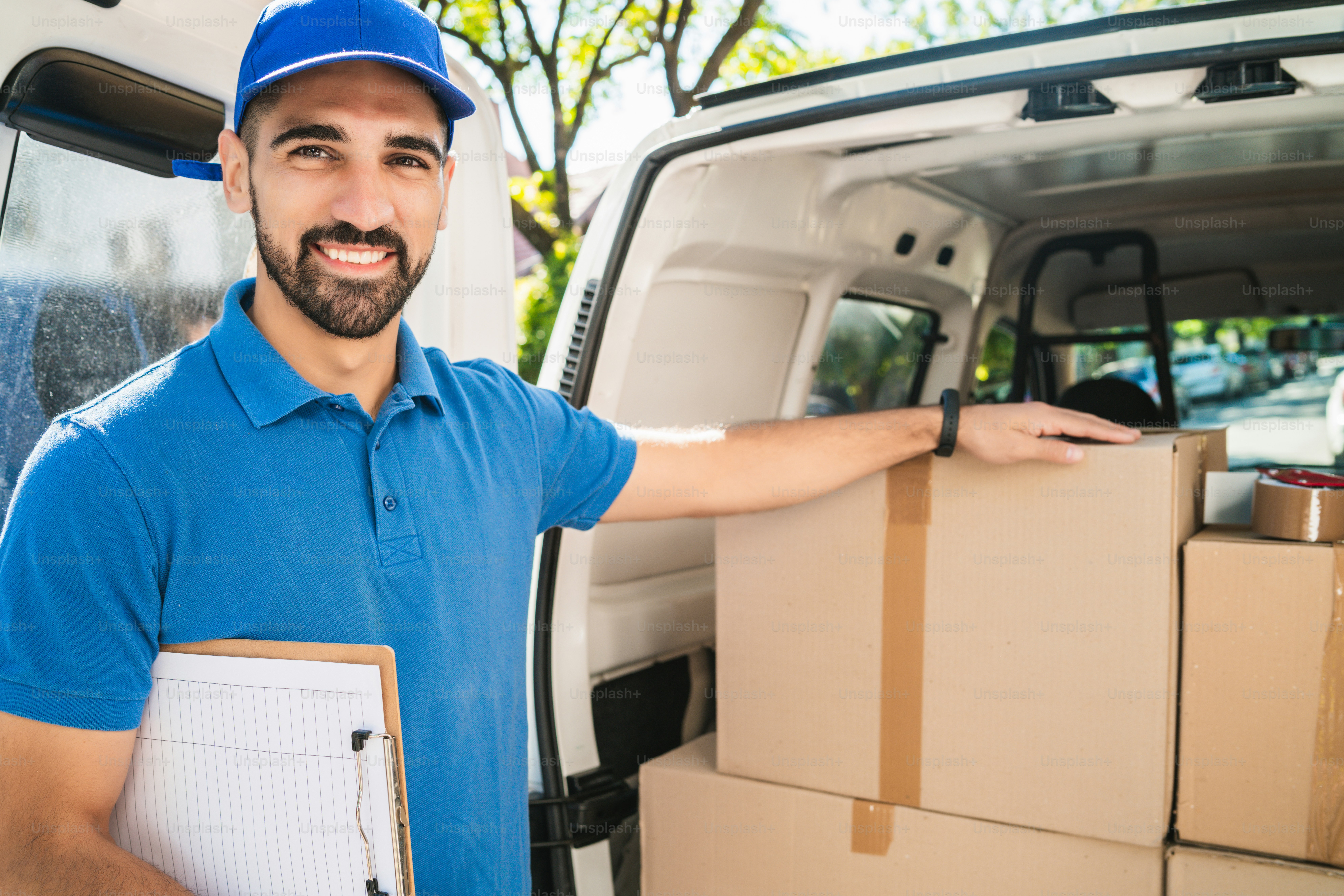 Portrait of a delivery man checking the products in checklist while standing right next to his van. Delivery and shipping concept.