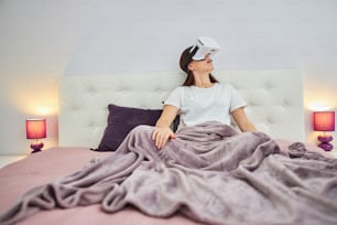 Amazed woman turning her head around the bedroom watching it through the augmented reality glasses