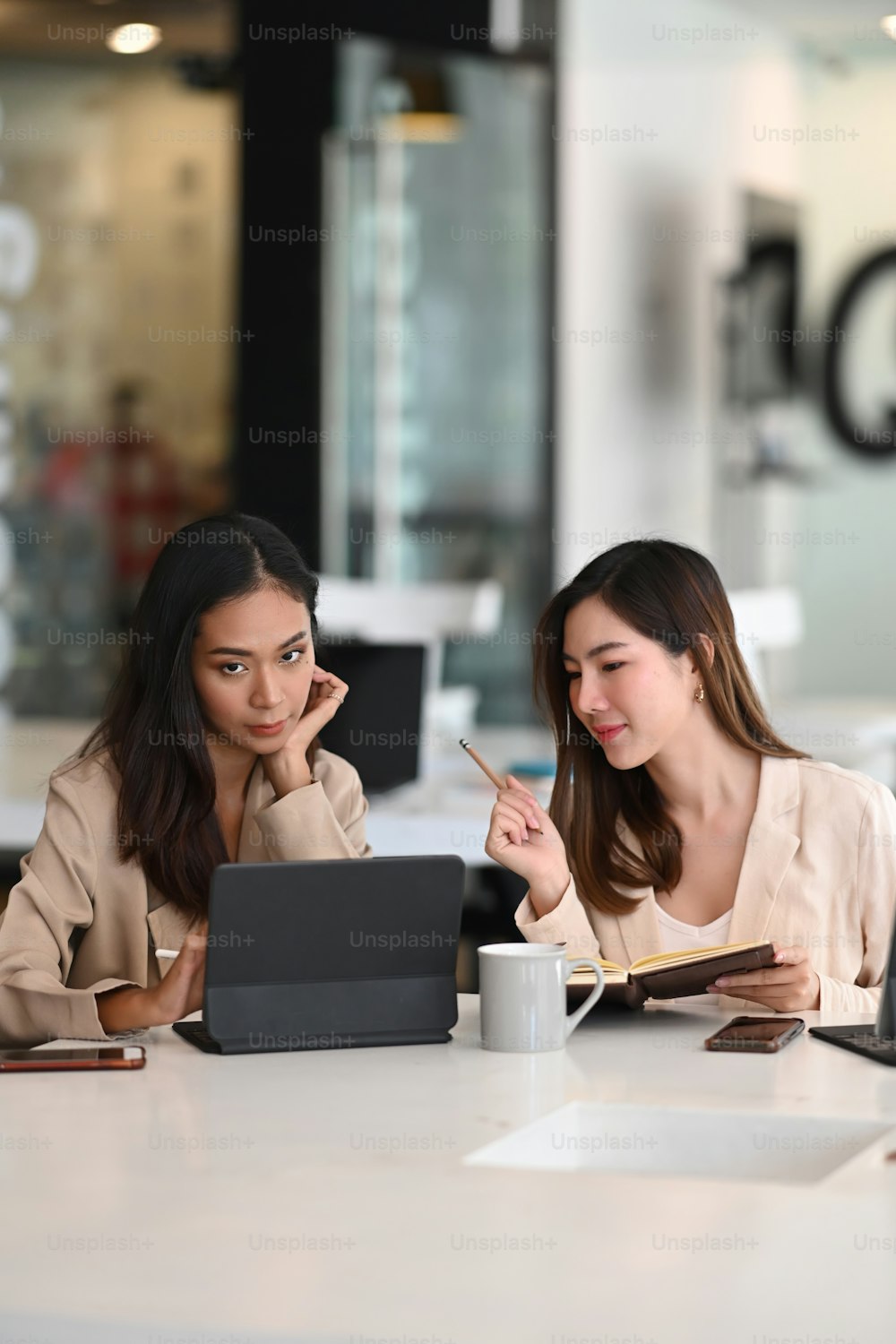Zwei Geschäftsfrauen arbeiten zusammen und diskutieren Projektpläne, während sie ein digitales Tablet im Büro verwenden.