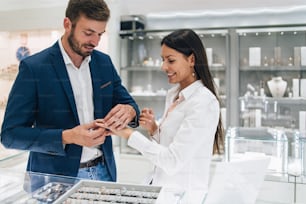 Beautiful couple enjoying in shopping at modern jewelry store. Close up shot of woman's hand with gorgeous expensive ring and bracelet.