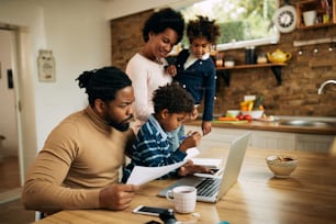 Black working father using laptop while being with his wife and kids at home.