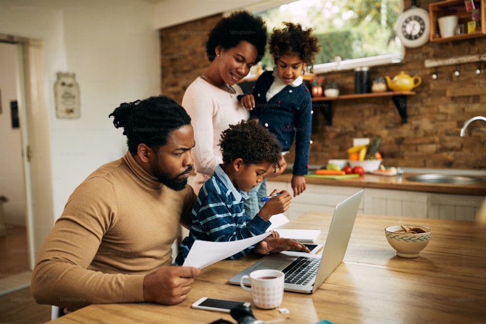 Schwarzer berufstätiger Vater, der Laptop benutzt, während er mit seiner Frau und seinen Kindern zu Hause ist.