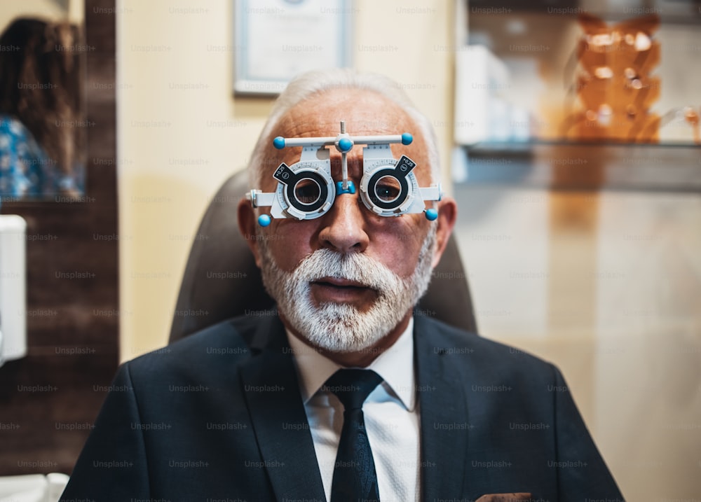 Elegant senior bearded man in optometry glasses receiving ophthalmology treatment. Doctor ophthalmologist checking his eyesight with modern equipment.