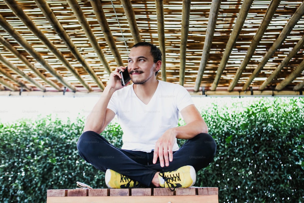 Mexican Man using smartphone sitting cross-legged, Home work and lifestyle concept in Latin America
