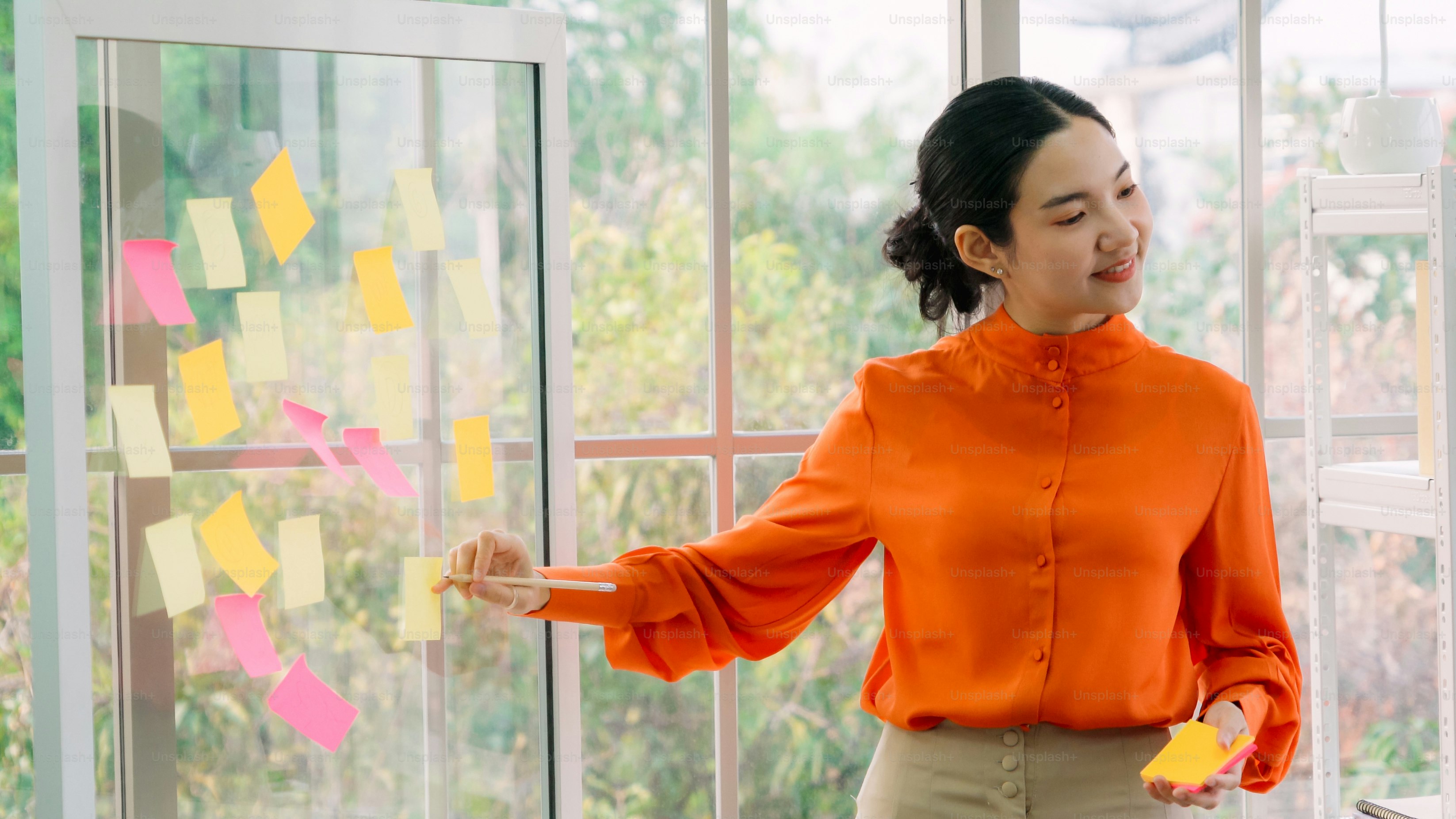 Business people work on project planning board in office and having conversation with coworker friend to analyze project development . They use sticky notes posted on glass wall to make it organized .
