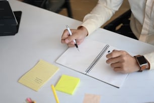 Abgeschnittene Aufnahme eines Geschäftsmannes, der einen Stift hält und Notizen auf einem Notizbuch macht.