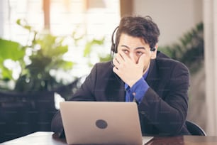 Asian businessman have action with a tired expression between using computer laptop. he cover face with hand upset from work in front of.