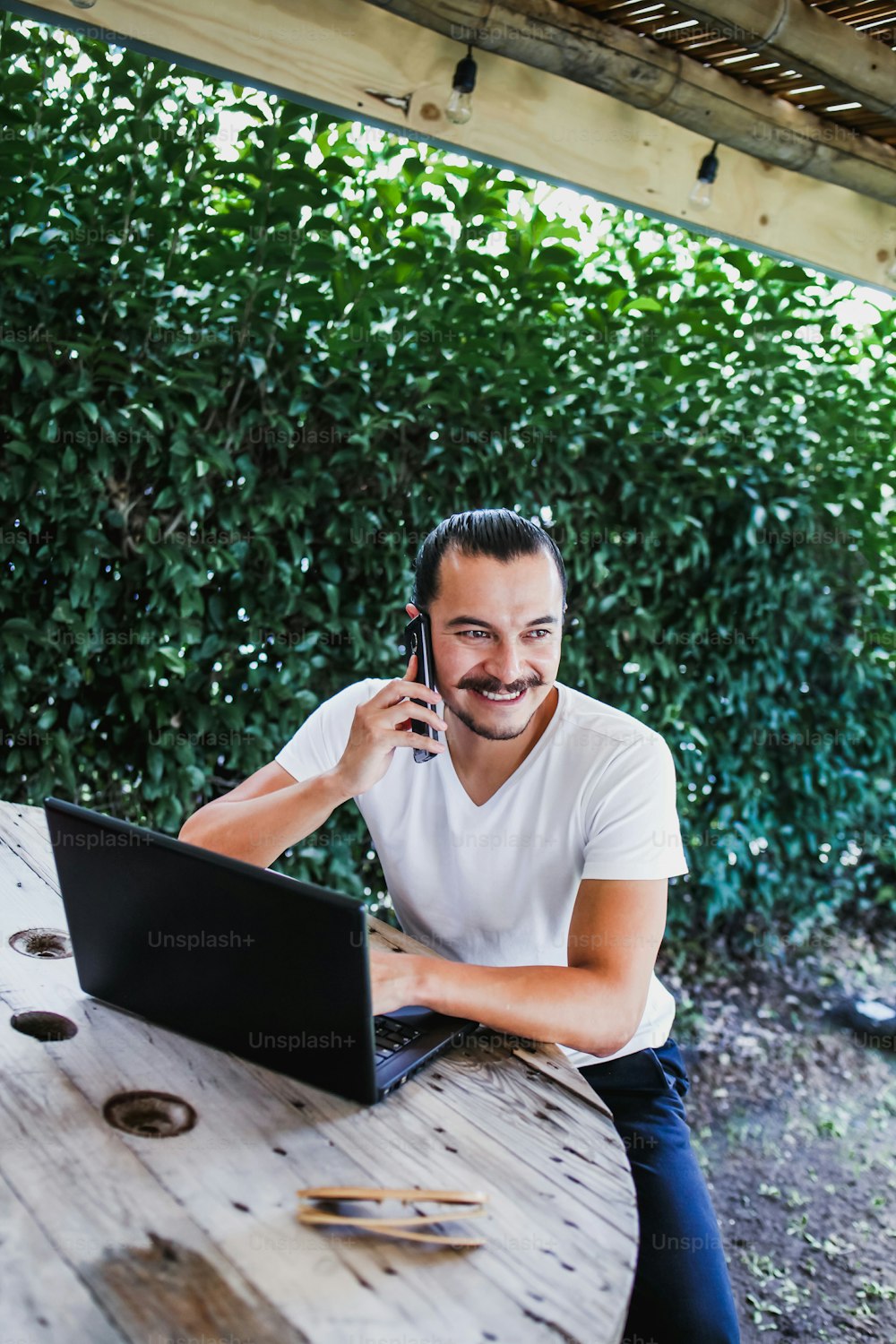 Lateinamerikanischer Mann mit Handy und Computer auf einer Terrasse in Mexiko-Stadt