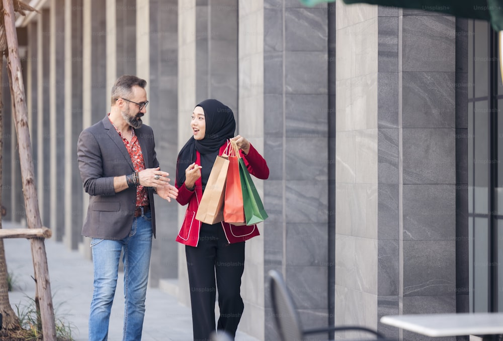 Mujer musulmana feliz y amigo del muchacho con la mano de la compra de la ciudad sosteniendo bolsas de papel