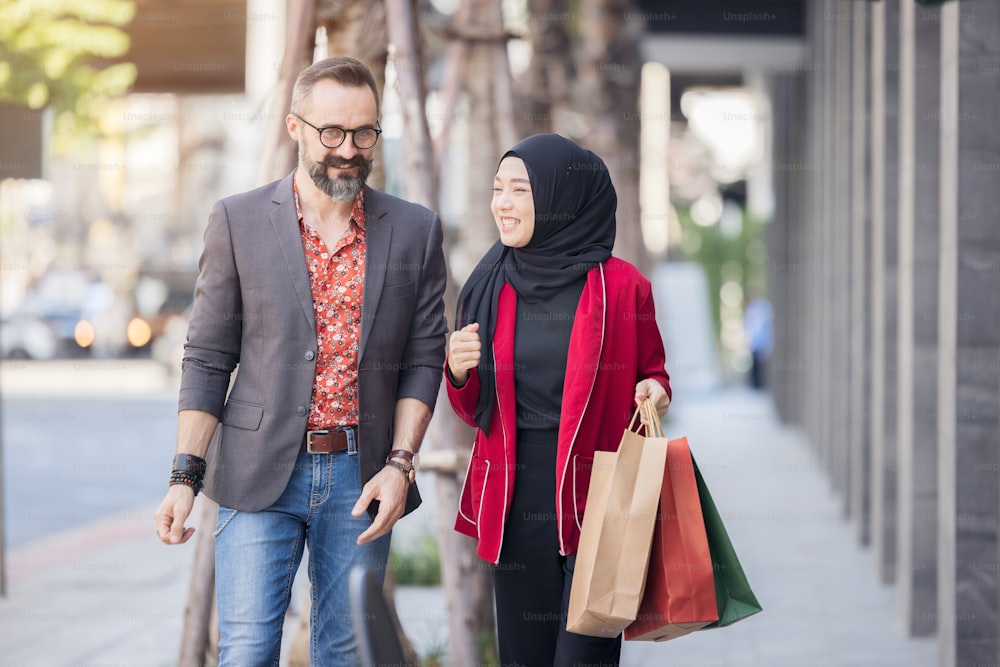 Mujer musulmana feliz y amigo del muchacho con la mano de la compra de la ciudad sosteniendo bolsas de papel