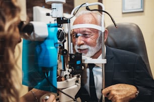 Elegante uomo barbuto anziano che riceve un trattamento oftalmologico. Medico oftalmologo che controlla la sua vista con attrezzature moderne.