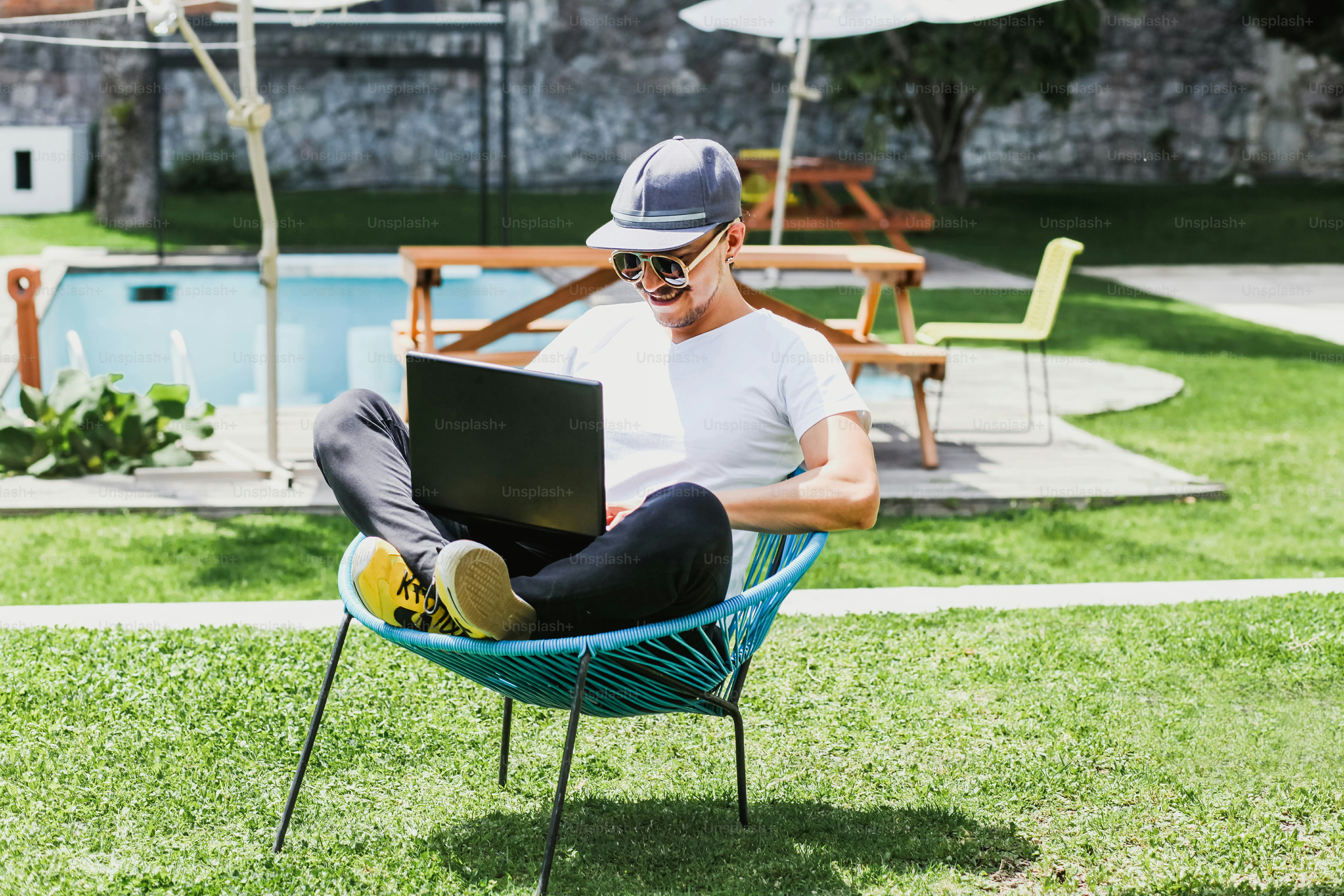 Hombre latino trabajando con computadora portátil al aire libre en una hermosa terraza usando un teléfono inteligente y una computadora sentado con las piernas cruzadas en el trabajo en casa en la Ciudad de México