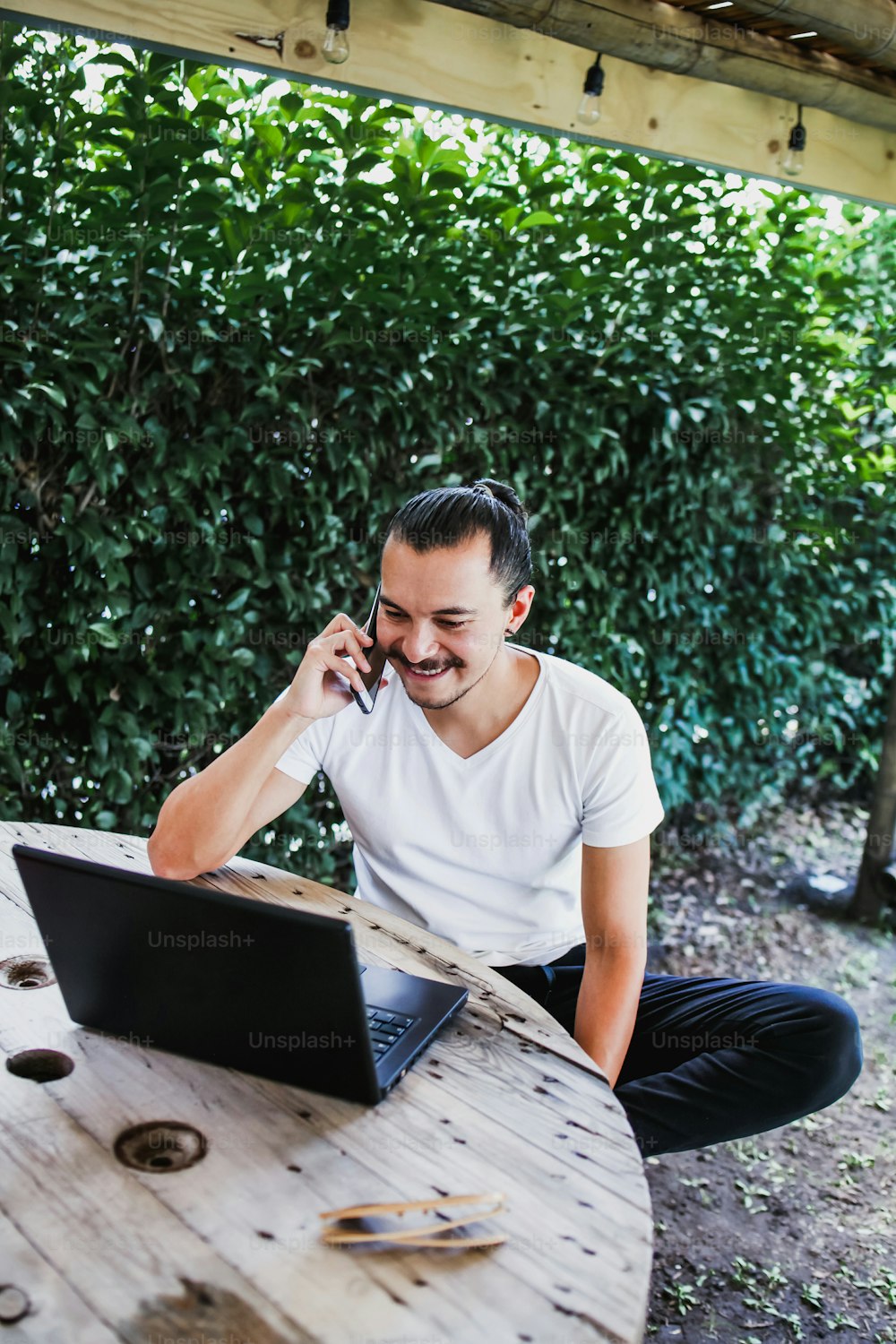 latin man using his mobile phone and computer in a home terrace in Mexico city