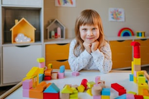 Little 4 years old girl playing with wooden cubes building a toy city