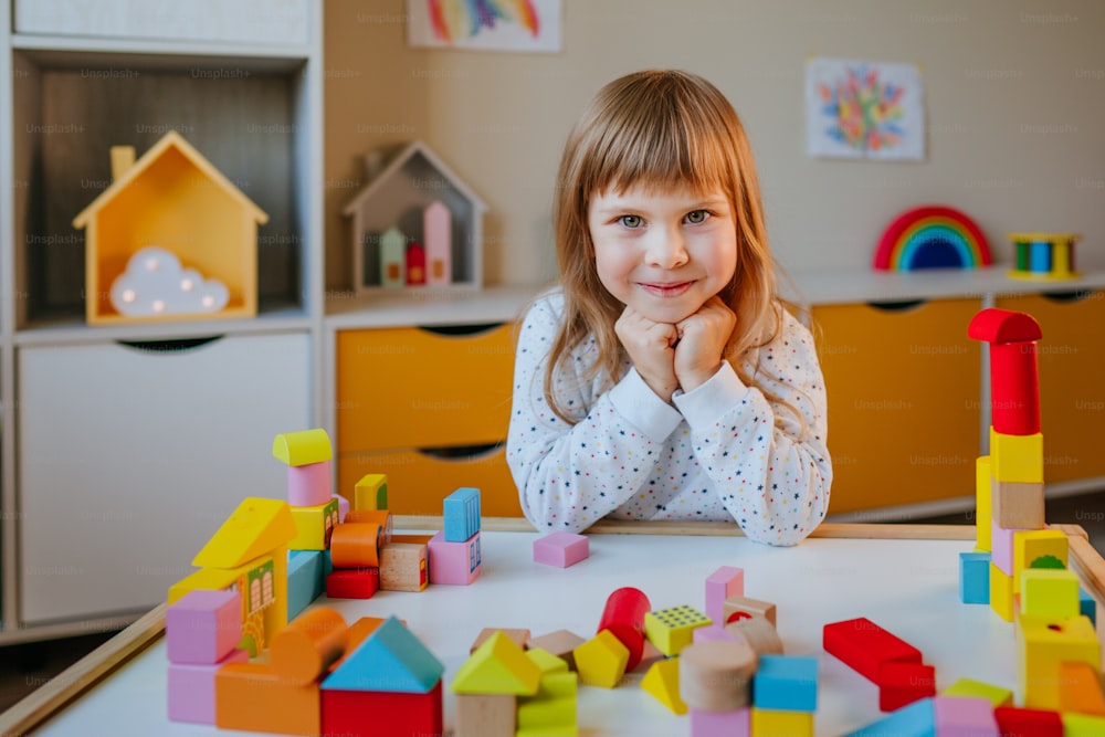 Menina pequena de 4 anos de idade que brinca com cubos de madeira construindo uma cidade de brinquedo