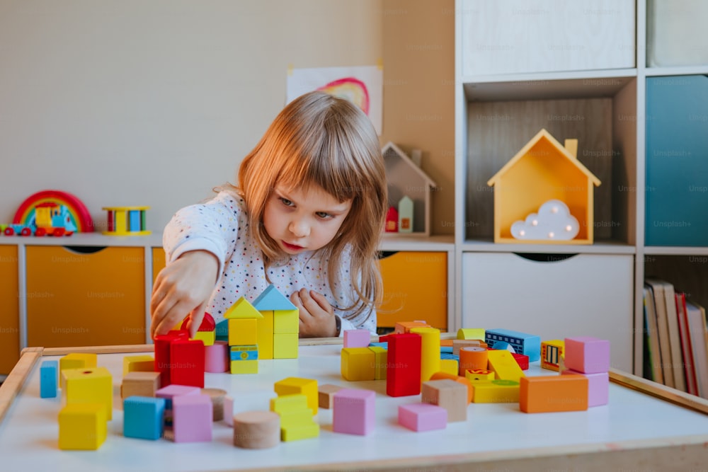 Menina pequena de 4 anos de idade que brinca com cubos de madeira construindo uma cidade de brinquedo