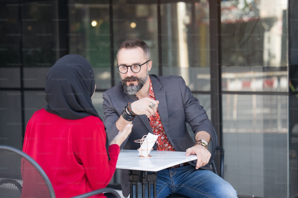 Donna d'affari musulmana asiatica in una caffetteria che parla con un cliente o un amico