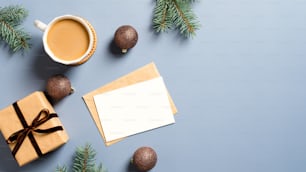 Christmas composition. Flat lay blank greeting card mockup, gift box, coffee cup, brown balls and pine tree branches on blue background.