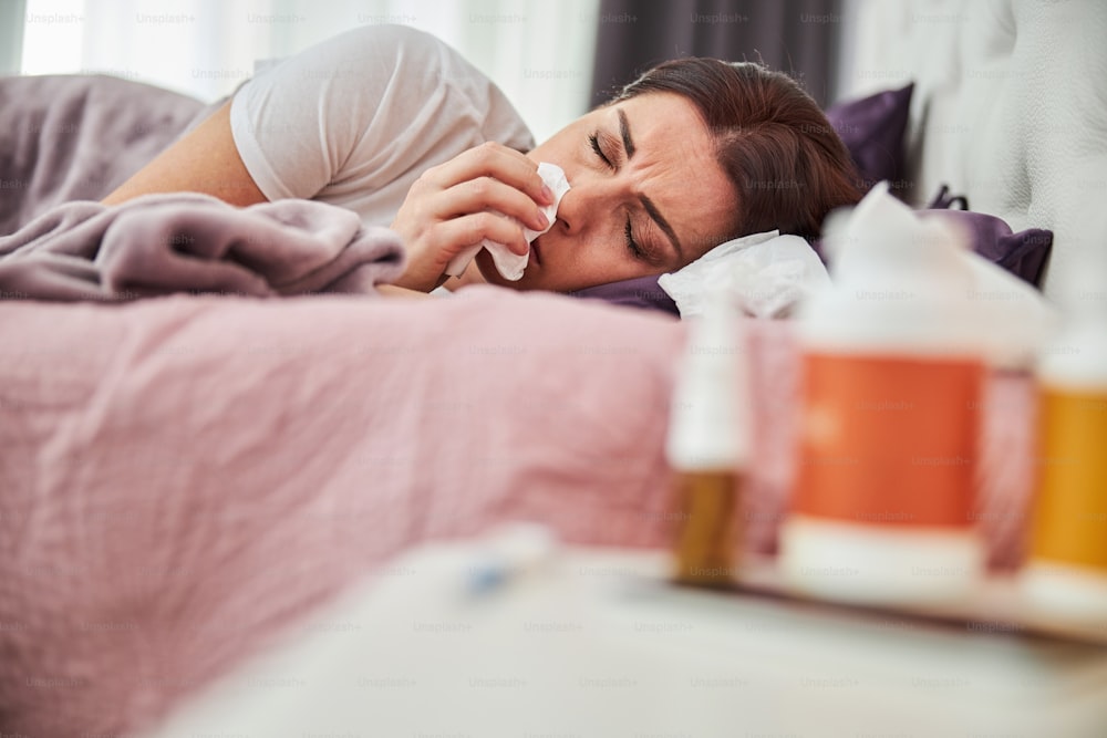 感染症にかかり、鼻水を出しながら枕で休む成人女性