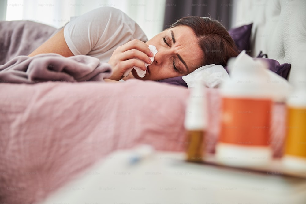 Adult lady catching an infection and resting on a pillow while having a running nose