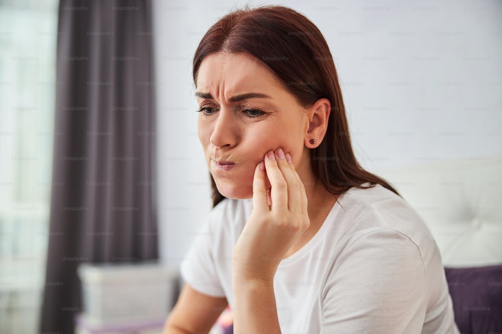 Close-up photo of a person touching her cheek and twisting her lips because of pain in her teeth