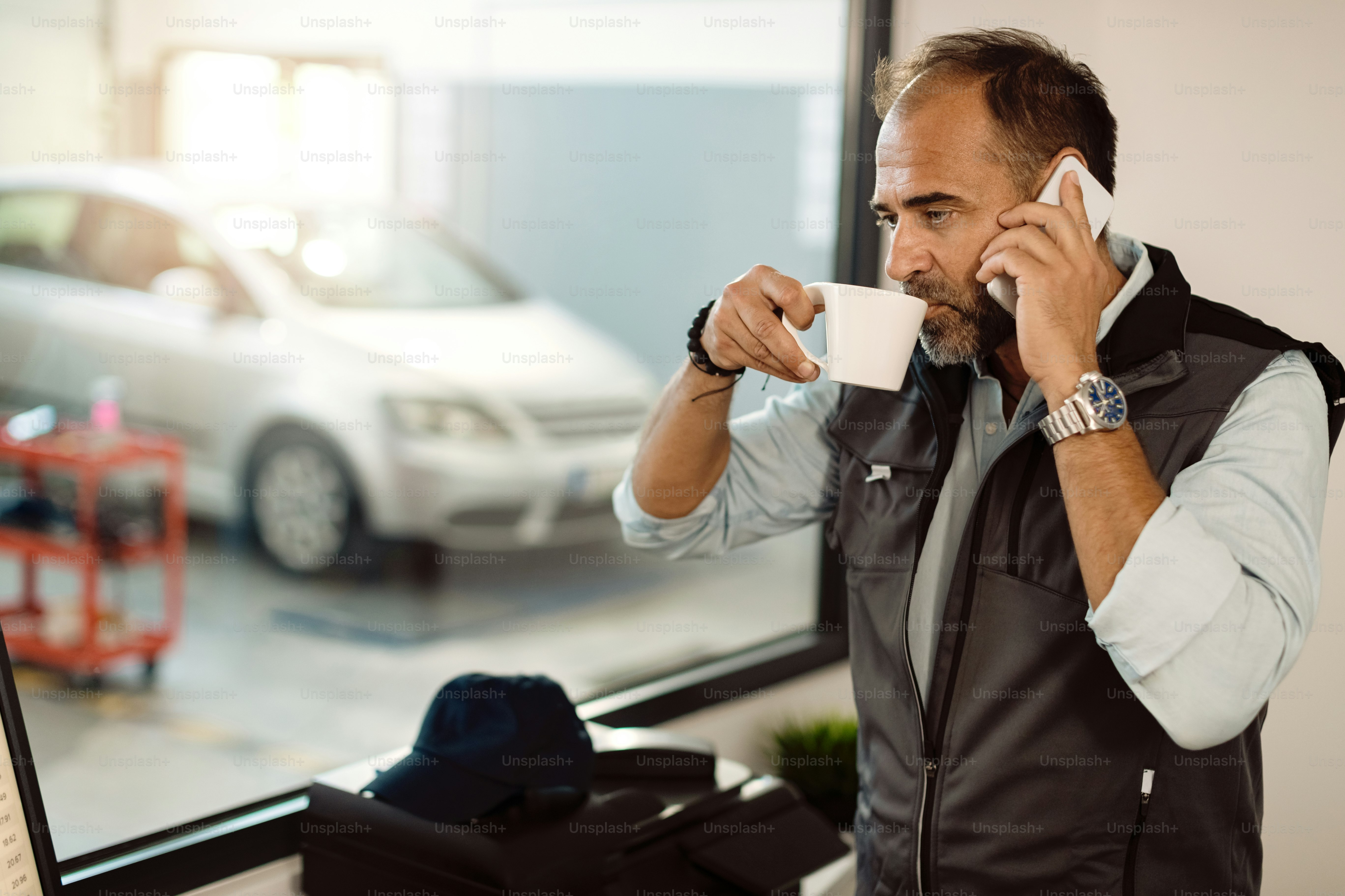 Auto mechanic drinking coffee while making a phone call at workshop's office.
