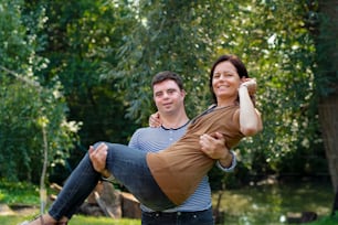 Portrait of happy down syndrome adult man carrying mother in arms outdoors in garden.