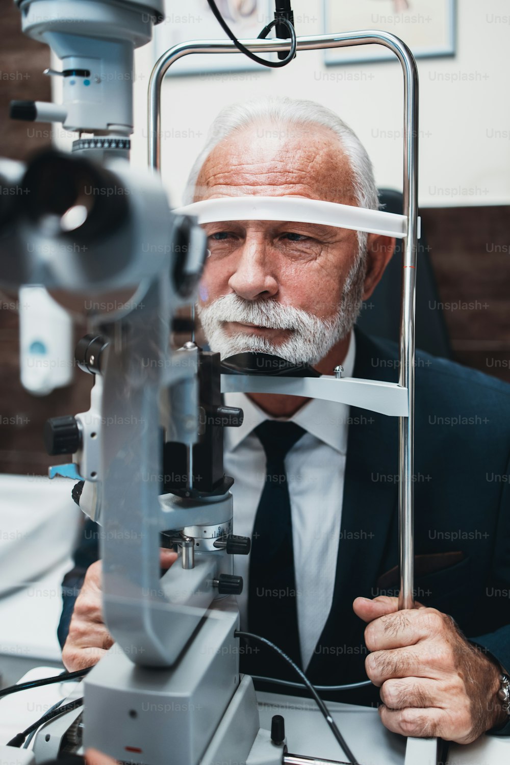 Elegant senior bearded man receiving ophthalmology treatment. Doctor ophthalmologist checking his eyesight with modern equipment.