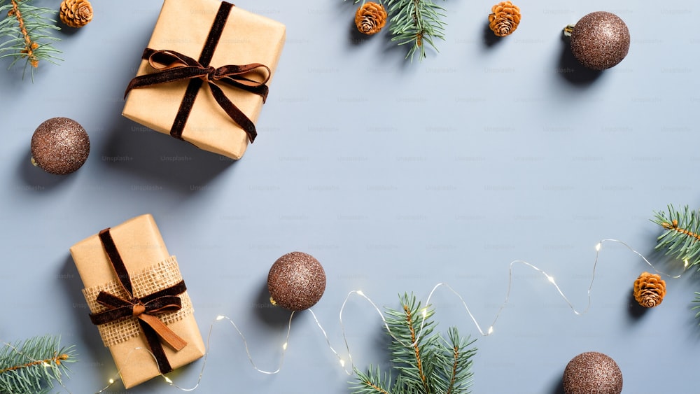 Cadeau de Noël et décorations avec des branches de pin sur fond bleu pastel. Pose à plat, vue de dessus. Cadre de Noël. Style minimaliste.