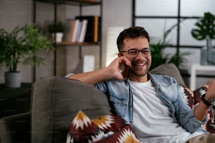 Young man talking on the phone while sitting on sofa. Happy man using the phone.