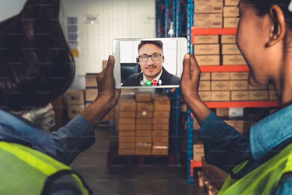 Warehouse staff talking on video call at computer screen in storage warehouse . Online software technology connects people working in logistic factory by virtual conference call on internet network .