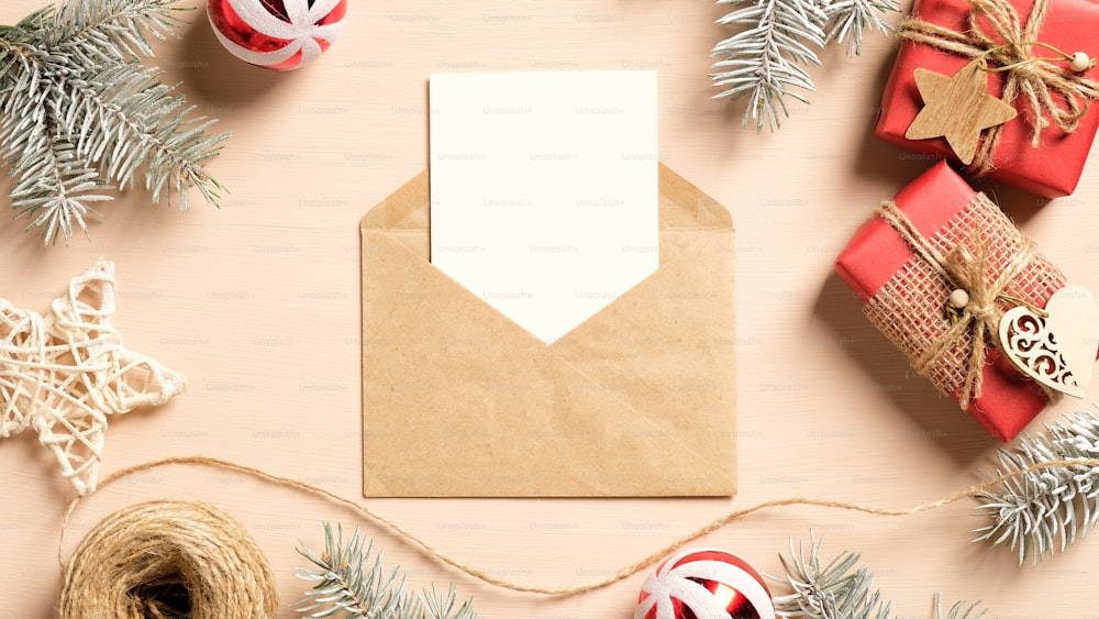 크리스마스 편지 개념입니다. 공예 종이 봉투, 크리스마스 선물, 나무 장식, 베이지색 배경에 소나무 가지에 있는 빈 종이 카드. 크리스마스 초대장 모형. 플랫 레이, 평면도.