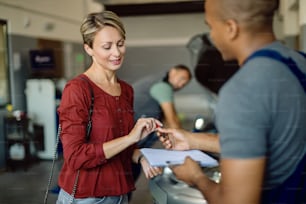 Cliente do sexo feminino assinando papelada depois que seu carro foi reparado na oficina de reparação de automóveis.